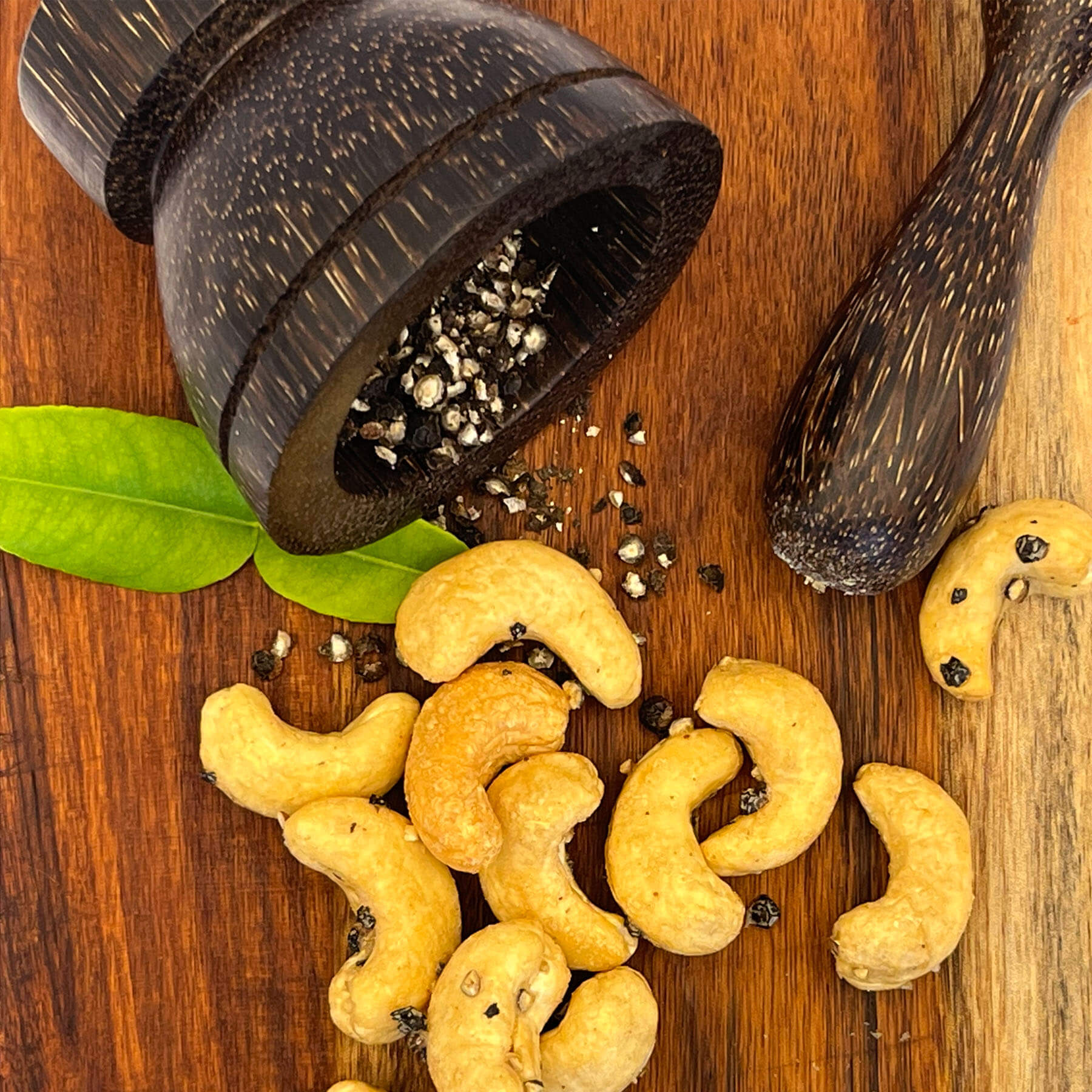 Geröstete Cashews mit schwarzem Kampot Pfeffer neben einem Mörser aus Kokosholz