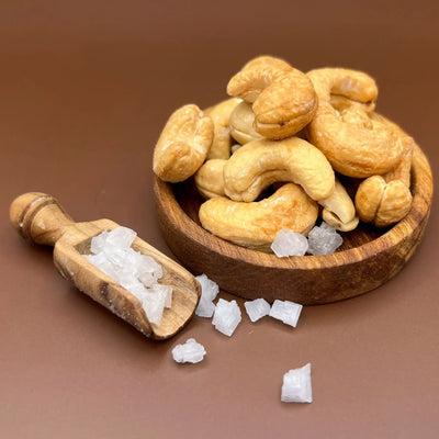 Geröstete Cashews in einer Holzschale mit grobem Meersalz in der Gewürzschaufel