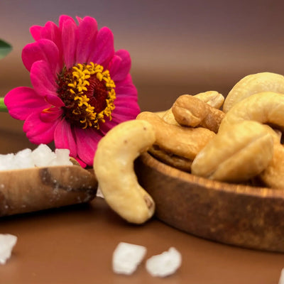 Cashews Sea Salt in der Kokosholzschale mit Meersalzflocken und pinker Blüte